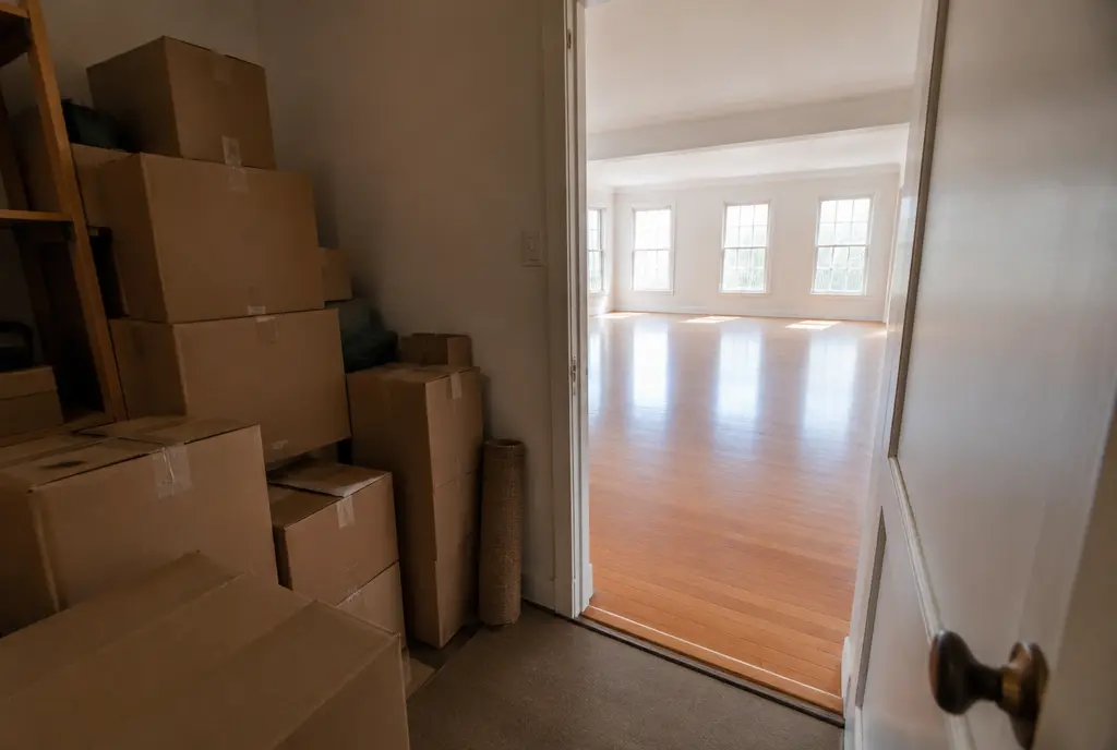 Doorway from a room crowded with boxes to a large bright empty room (AI-generated image)