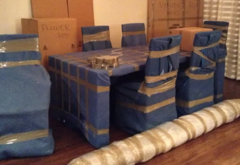 Table and chairs wrapped in moving blankets, ready for transport — real photo